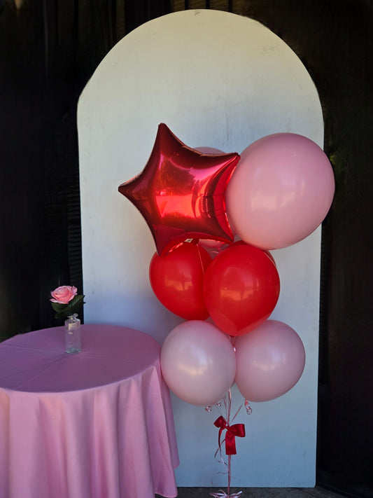 Bouquet of red and pink balloons with a star-shaped balloon on a white arch and pink tablecloth.